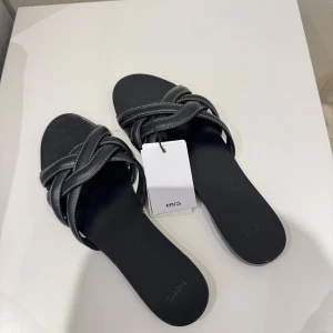 ÄKTA LÄDER Mango sandaler/tofflor - Stilrena svarta sandaler från MNG med breda, flätade remmar och kontrastsömmar. Platt sula och öppen tå gör dem perfekta för varma dagar. Snygg och enkel design som passar till många outfits. ÄKTA LÄDER, storlek 40, NYPRIS 520kr!! 🥰