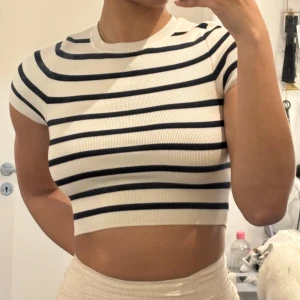 Randig croppad topp från Zara - Säljer en croppad topp från Zara i vitt med svarta horisontella ränder. Toppen har korta ärmar och är ribbad i materialet, vilket ger en snygg och bekväm passform. Perfekt till sommaren!