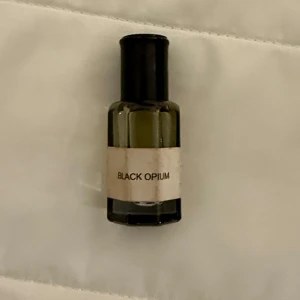 Mini Black Opium parfym - Säljer en mini parfym med doften Black Opium. Flaskan är mörkgrön med svart kork och har en enkel vit etikett med texten 'Black Opium'. Perfekt storlek att ta med i väskan.