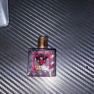 Versace Eros Flame parfym - Versace Eros Flame parfym i en liten, fyrkantig röd flaska med guldlock. Flaskan har ett Medusa-huvud i relief och klassiskt Versace-mönster runt kanterna. Perfekt för dig som gillar lyxiga och intensiva dofter.