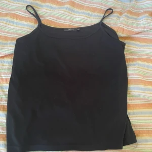 Svart linnetopp från XLNT Woman - En enkel och stilren svart linnetopp från XLNT Woman med tunna axelband. Perfekt att matcha med jeans eller kjol för en clean look. Tillverkad i mjukt material som känns skönt mot huden.