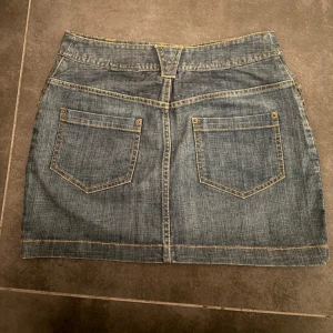 Jeanskjol från H&M - Klassisk blå mini jeanskjol från H&M i modell med två bakfickor och bälteshällor. Kjolen har synliga kontrastsömmar och stängs med knapp och dragkedja framtill. Perfekt för en trendig look. 💓