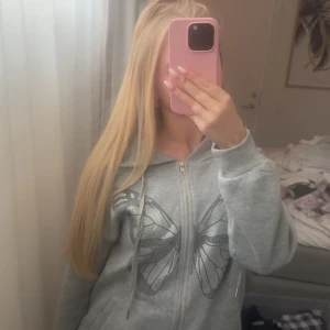 Grå hoodie med fjärilstryck - Säljer en grå hoodie med dragkedja och stort fjärilstryck. Tröjan har huva och långa ärmar. Supermjuk och skön att ha på sig! I bra skick då den inte är använd alls många gånger.