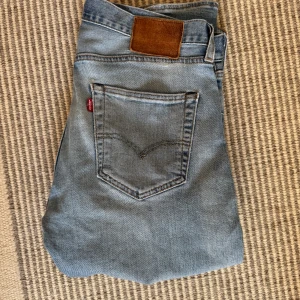 Ljusblåa Levis jeans - Säljer ett par klassiska ljusblåa Levis jeans med femficksdesign och brun läderpatch bak. Byxorna har normal passform och raka ben, perfekt för en avslappnad stil. E:31 L34