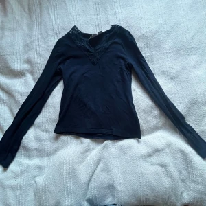 Marin blå långärmad topp med spets från Gina Tricot - Säljer en marin blå långärmad topp från Gina Tricot med v-ringning och fina spetsdetaljer vid halsen. Perfekt att styla till olika outfits och superbekväm att bära.