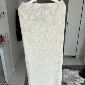 Plisserad vit maxikjol från Gina Tricot - Säljer en naturvit plisserad maxikjol från Gina Tricot. Kjolen har ett vågigt, strukturerat tyg och rak passform. Perfekt för dig som gillar stilrena och trendiga plagg. Resår i midjan och prislappen kvar!