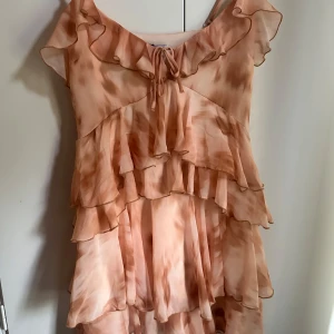 BERSHKA klänning - Superfin kortklänning från Zara i ljusrosa med volanger och omlottkänsla. Klänningen har tunna axelband, v-ringning med knyt och flera lager volanger som ger en flowy look. Perfekt för sommarens alla tillfällen!