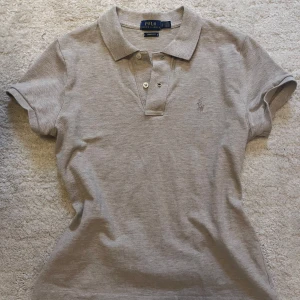 Beige polotröja från Polo Ralph Lauren - Beige polo t-shirt Ser lite gråaktig ut på bilderna men mer beige i verkligheten. Inga fläckar eller hål som jag vet om Knappt använd Skriv vid frågor💓💓