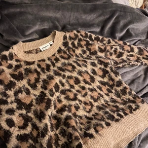 Leopardmönstrad stickad tröja från Kappahl - Säljer en supermjuk stickad tröja från Kappahl i beige med leopardmönster i brunt och svart. Tröjan har rund halsringning och långa ärmar med ribbade muddar. Perfekt för dig som vill sticka ut lite extra!