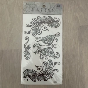 Svart temporär tatuering med paisleymönster - Ett ark med temporära tatueringar i svart med detaljerade paisley- och fjärilsmönster. Perfekt för att skapa en unik look tillfälligt. Mönstren är dekorativa och har fina linjer och snirkliga detaljer.