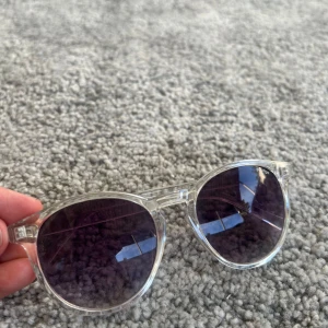 Transparenta solglasögon med lila tonade glas - Snygga solglasögon med transparent båge och runda, lila tonade glas. Perfekt accessoar för soliga dagar och en modern look. Lätta och bekväma att bära, passar de flesta ansiktsformer.