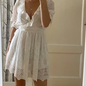Vit klänning   - Superfin vit kortklänning med omlottmodell och broderade blommor. Klänningen har volangkant längs urringningen och ärmarna, samt halvlånga ärmar. Perfekt för sommarens alla tillfällen och midsommarfirande. Perfekt till studenten!