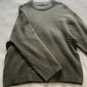 Olivgrön stickad tröja från 157 - Mysig olivgrön stickad tröja från 157 med rund halsringning och långa ärmar.