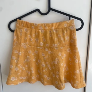 Gul blommig kjol från H&M - Superfin gul kjol från H&M med vita och rosa blommor. Kjolen har en lätt utställd form och är perfekt för dig som gillar färgglada plagg. Mjuk och skön med resår i midjan. Perfekt för vår och sommar!