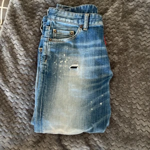 Blå Dsquared2 jeans med slitningar  - Säljer ett par blå jeans från Dsquared2 med lite  slitningar. Jeansen har klassisk femficksdesign, knappgylf och patch på bakfickan. De har en något tvättad look och är raka i modellen. Storleken är W27-28 sitter jättebra på båda. L30 ny pris cirka 3000 mitt pris 899. Hör av er vid minsta fundering. Pris går att diskutera!