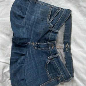 Mörkblå jeansshorts med volangkant - Snygg mörkblå lågmidjad jeanskjol med volangkant nedtill. Klassisk femficksmodell med knapp och dragkedja framtill. Perfekta för en trendig och avslappnad look. Gjort själv från ett par jeans men snyggt sydd och kommer inte gå i sönder. Passar mig med storlek 34/36! Pris kan diskuteras vid snabb affär 