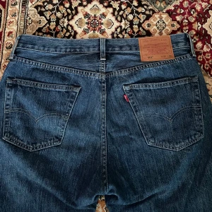 Levi's 501 blå jeans - Klassiska blå Levi's 501 jeans med raka ben och femficksdesign. Jeansen har normal passform, knappgylf och tydlig läderpatch bak i midjan. Perfekta för en tidlös denimlook.