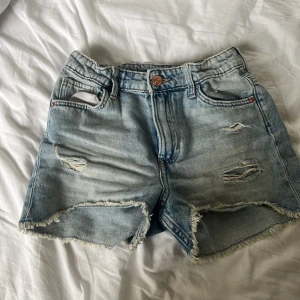 Ljusblå slitna jeansshorts - Säljer ett par ljusblå jeansshorts med fransig kant och slitna detaljer framtill. Lite sliten på bakfickorna annars i bra skick💕 Klassisk femficksmodell med knapp och dragkedja. Perfekta för sommaren☀️