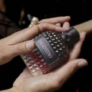 Parfym från Valentino - Snygg parfymflaska från Valentino med ett unikt, nitat mönster. Flaskan har en mörk kork och en elegant design som utstrålar lyx och stil. Perfekt för den som vill ha en doft med attityd och klass.