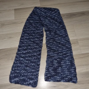 Mörkblå stickad halsduk - Säljer en mysig mörkblå stickad halsduk med ett melerat mönster i olika blå nyanser. Perfekt för att hålla värmen under kyliga dagar. Halsduken är bred och lång, vilket gör den extra skön att svepa runt halsen.