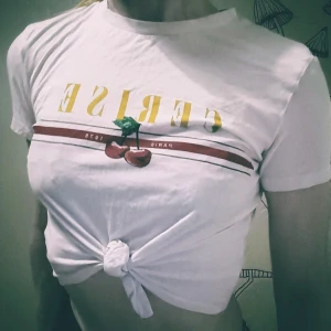 Knyt tshirt - Sommrig tshirt som går att knyta vid midjan för en extra het look i sommar. Klassiska körsbär som tryck och text. Den här blir aldrig gamal och passar till det mesta om det så är en utekväll eller en mer avslappnad chill dag med serier och skräpmat. 