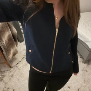 Mörkblå jacka från Holly & Whyte - Snygg mörkblå jacka från Holly & Whyte med dragkedja och guldknappar. Jackan har en stilren design med långa ärmar och är perfekt för en chic look. Passar bra till både jeans och kjol. Priset kan jag sänka om de är en snabb affär