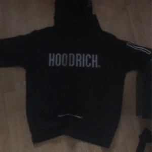 Svart hoodie från Hoodrich - Säljer en svart hoodie från Hoodrich med tryck på framsidan. Den har långa ärmar och en klassisk huva. Perfekt för en casual look.