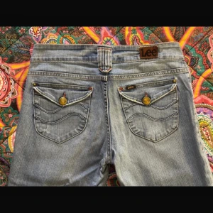 Ljusblå jeans från Lee - Snygga ljusblå jeans från Lee med bootcut-stil. De har klassiska fyra fickor och en knappgylf. Bakfickorna är dekorerade med knappar och sömmar. Perfekta för en avslappnad look. Inga defekter. Storlek S/M
