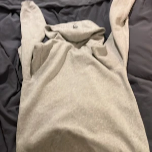 Grå hoodie från Sail Racing - Säljer en grå hoodie från Sail Racing med dragkedja och huva. Den har en broderad logga på bröstet och är tillverkad i ett mjukt material. Perfekt för en avslappnad stil.