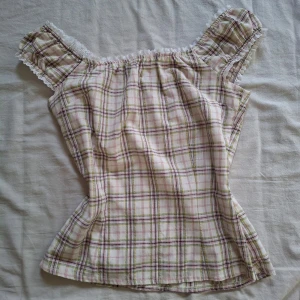 Rutig offshoulder blus med spetsdetaljer - Charmig rutig blus i offshoulder-stil med spetsdetaljer längs kanterna. Blusen har en mjuk och luftig passform, perfekt för varma dagar. Rutigt mönster i beige, rosa och grönt ger en klassisk look. Sparsamt använd ♡