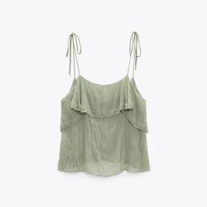 Grön topp  med volangdetaljer - Säljer ett luftigt och stilrent grönt linne i chiffong med tunna axelband och volangdetaljer. Perfekt för varma dagar eller sommarens fester. Lånade bilder och det är oanvänd skriv för bilder på