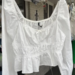 Vit blus från H&M - Säljer en söt vit blus från H&M med puffärmar och volangdetaljer och långärmad design. Blusen har en v-ringad hals och är perfekt för en stilren look. Passar bra till både jeans och kjol. Aldrig använd🌸💕🌸💕🤩