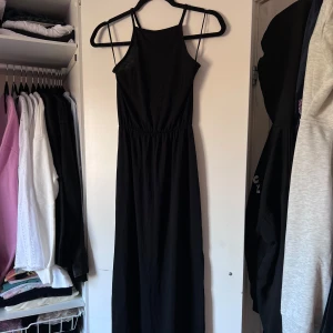 Svart långklänning från Bik Bok - Snygg svart långklänning från Bik Bok i en enkel och stilren design. Klänningen har smala axelband, slits på både vänster och höger sida och en rak passform som ger en elegant look. Perfekt för olika tillfällen och lätt att matcha med accessoarer. Önskar du veta exakta mått? Tveka inte att höra av dig!