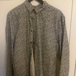 Blommig skjorta från H&M - Snygg blommig skjorta från H&M i svart och vitt. Skjortan har en slim fit passform och långa ärmar med knappar framtill. Perfekt för att ge en stilren touch till din outfit.