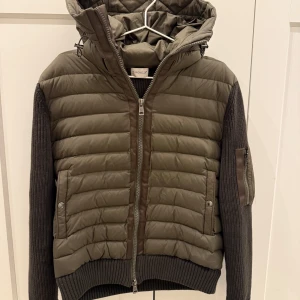 Moncler cardigan - Snygg grön quiltad jacka från Moncler med huva och dragkedja. Jackan har stickade ärmar och ribbade muddar. Perfekt för vårvädret som närmar sig med sin kombination av stil och funktionalitet. Jackan passar mig perfekt som är 183cm lång. Storlek L men passar M. Inga defekter i topp skick. Hör av er vid frågor mvh Lucas!