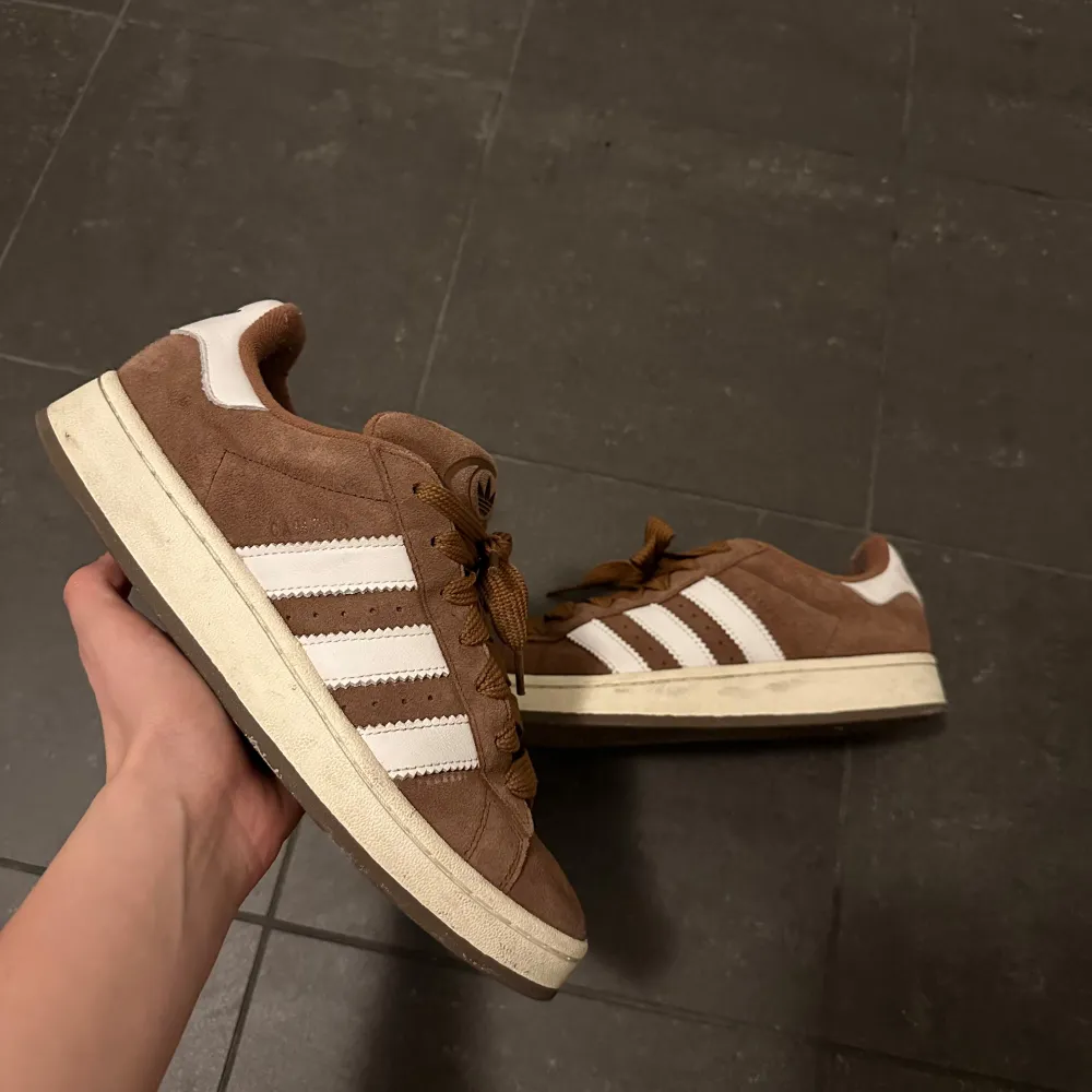 Säljer ett par bruna Adidas sneakers med vita ränder och detaljer. Skorna har en klassisk design med snörning och en bekväm sula. Perfekta för en avslappnad stil.9/10 sick stilrena passar alla outfits och är skit snygga 🔥, de är super sick och om det är några frågor är det bara att höra av sig,de är i materialet mocha och därför blir dom så unika och speciella,OBS de är stl 42 men passar 43 funkar till både herr och dam.🙌🔥✅☑️. Kengät.