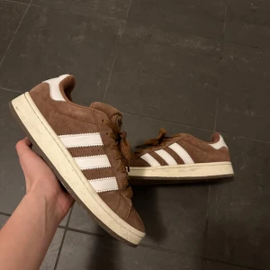  Adidas campus  - Säljer ett par bruna Adidas sneakers med vita ränder och detaljer. Skorna har en klassisk design med snörning och en bekväm sula. Perfekta för en avslappnad stil.9/10 sick stilrena passar alla outfits och är skit snygga 🔥, de är super sick och om det är några frågor är det bara att höra av sig,de är i materialet mocha och därför blir dom så unika och speciella,OBS de är stl 42 men passar 43 funkar till både  herr och dam.🙌🔥✅☑️