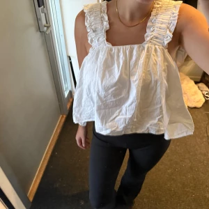 Vit blus från NA-KD - Säljer en söt vit blus från NA-KD med volangdetaljer på axelbanden. Blusen är kortare framtill 