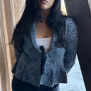 Mönstrad blå kofta med knytband - Säljer en snygg blå kofta  med ett geometriskt mönster i svart. Koftan har långa ärmar och ett knytband framtill för en stilren look. Perfekt för att lägga till lite mönster i din outfit!