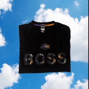 Svart t-shirt från Boss x NBA - Snygg svart t-shirt från Boss i samarbete med NBA. Den har ett coolt Lakers-tryck och BOSS-logga på framsidan. Perfekt för basketfans och streetwear-entusiaster.