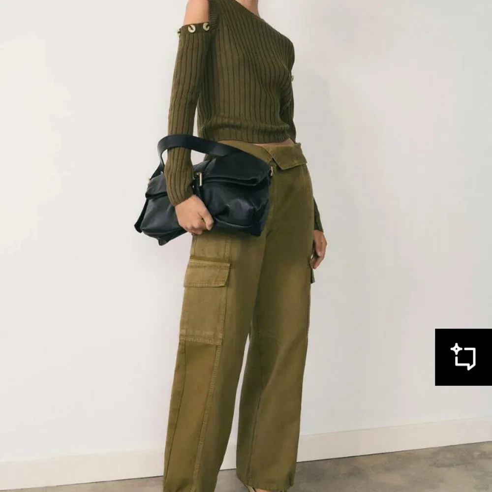 Snygg olivgrön ribbad tröja med offshoulder-design och dekorativa knappar vid axlarna. Perfekt för en trendig look med sin croppade passform och långa ärmar.. Neuletakit & Villapaidat.