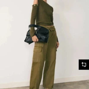 Olivgrön ribbad offshoulder tröja - Snygg olivgrön ribbad tröja med offshoulder-design och dekorativa knappar vid axlarna. Perfekt för en trendig look med sin croppade passform och långa ärmar.