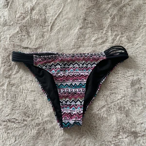 Mönstrade bikiniunderdel från Censored - Snygg bikiniunderdel från Censored med färgglatt zigzag-mönster i rosa, svart, vit och turkos. Sidorna har coola svarta banddetaljer som ger en trendig look. Perfekt för stranden eller poolen! Materialet är mjukt och stretchigt syntet för skön passform.