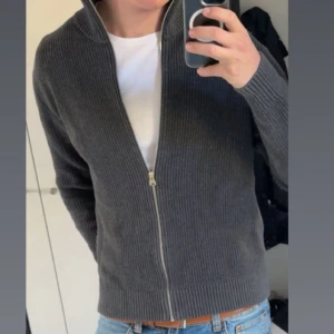 Stickad cardigan  - Säljer en mörkgrå stickad kofta från Cubus i storlek L. Koftan har ribbad struktur, hög krage och hel dragkedja. Den är bomull och i nyskick, tvättad ca 3 ggr. Säljer då den är lite för liten. För referens är jag 190cm 95 kg. Tveka inte med att höra av dig vid frågor m.m, pris kan diskuteras vid smidig affär 🤩