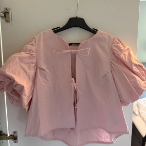 Rosa puffärmad blus från Gina Tricot - Supersöt ljusrosa blus från Gina Tricot med stora puffärmar och knytning framtill. Blusen har en rak passform och är tillverkad i ett mjukt bomullstyg. Perfekt för dig som gillar volym och romantiska detaljer. Toppen är använd en eller två gånger men kommer inte längre till användning. Köpt för 500kr, pris kan diskuteras💕