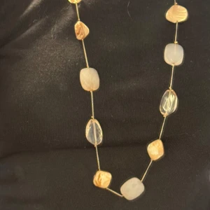 Långt halsband med pärlor i silver och beige - Unikt långt halsband med oregelbundna pärlor i guld, beige och transparent. Pärlorna är facetterade och sitter på en tunn kedja i silverfärg. Perfekt för dig som vill ha ett smycke som sticker ut och ger en cool touch till din outfit.