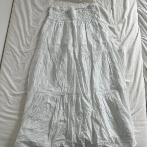 Vit långkjol med broderade blommor - Supersöt vit långkjol från Gina Tricot med broderade blommor och smock i midjan. Kjolen är lite skrynklig, bara använt en gång.