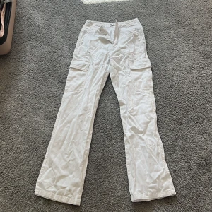 Vita cargobyxor från Zara, strl 34 - Säljer ett par vita cargobyxor från Zara i storlek 34. Byxorna har raka ben, flera fickor på sidorna och klassisk cargostil. De är tillverkade i bomull och har en avslappnad passform som är både snygg och bekväm.