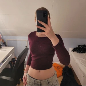 Vinröd croppad topp med snörning - Säljer en vinröd långärmad topp med croppad passform och snygg snörning i ryggen. Tunn och mjuk, perfekt att styla med jeans eller kjol. Toppen har en enkel rund hals och är figurnära, vilket ger en modern och trendig look.