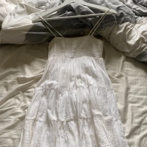 Vit sommarklänning från Gina Tricot - Superfin vit klänning från Gina Tricot med smock upptill och tunna axelband. Klänningen har en luftig, volangig kjol i flera lager och är perfekt för varma dagar. Använt två gånger så den är i mycket fint skick. Köpt för 399💕💕